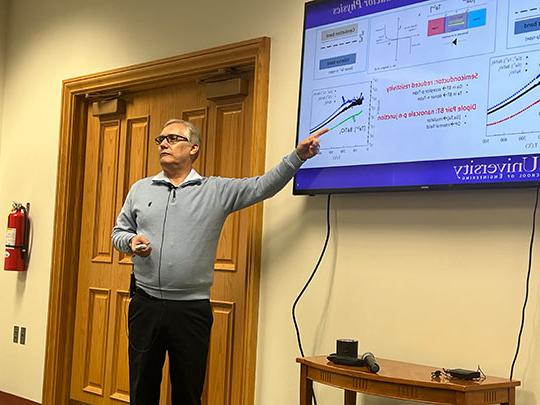 man with glasses making presentation in front of TV screen